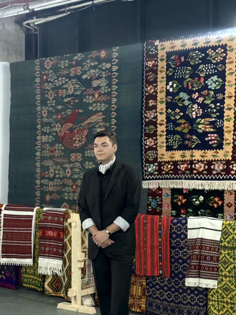 Andrei Fășie in front of traditional Gorj carpets and textiles